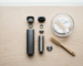 Disassembled dry herb vaporiser with a small brush, cotton swabs and a glass dish laid out on a light wooden surface